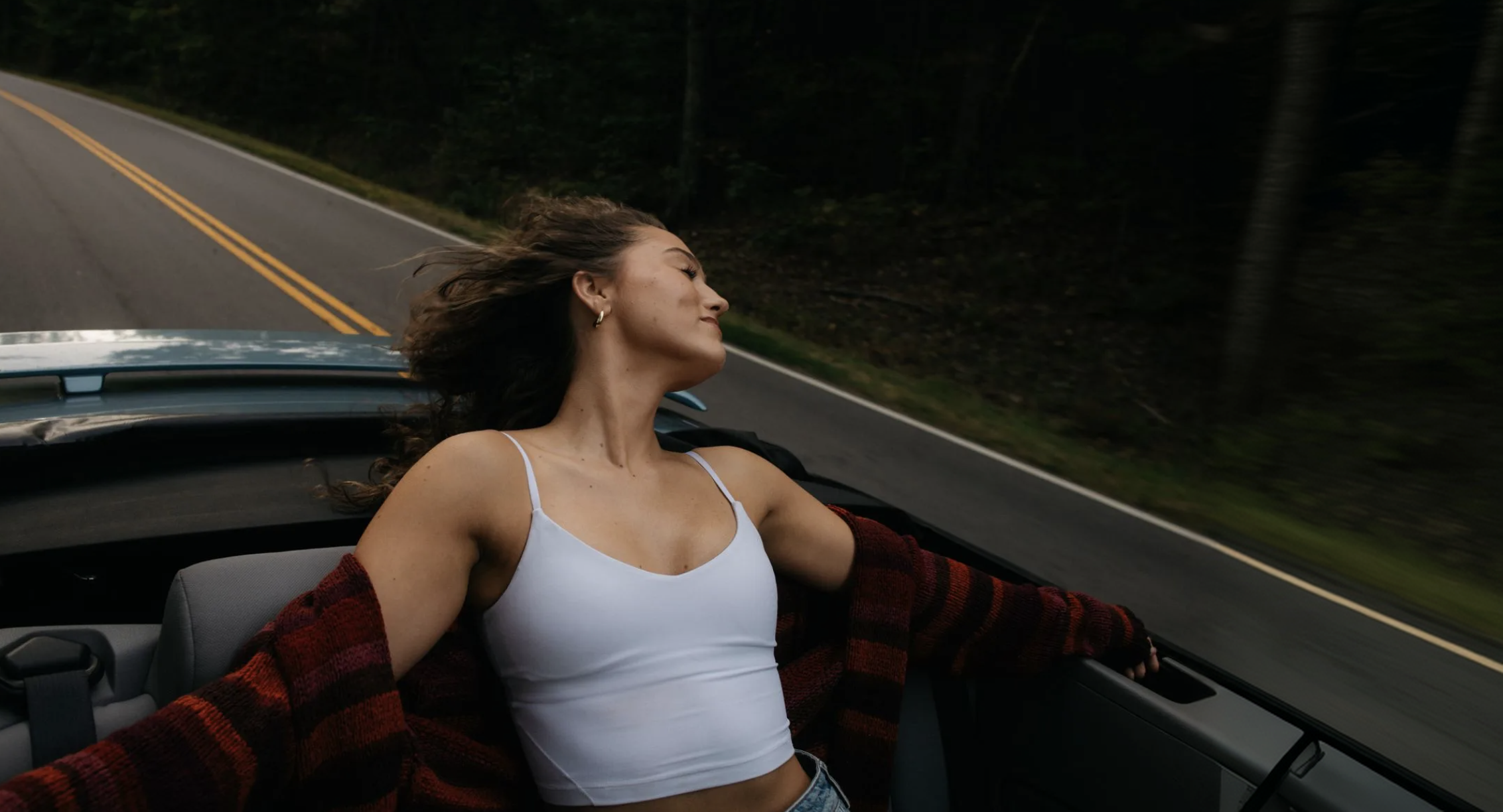 A woman relaxing in a moving convertible on a forest road